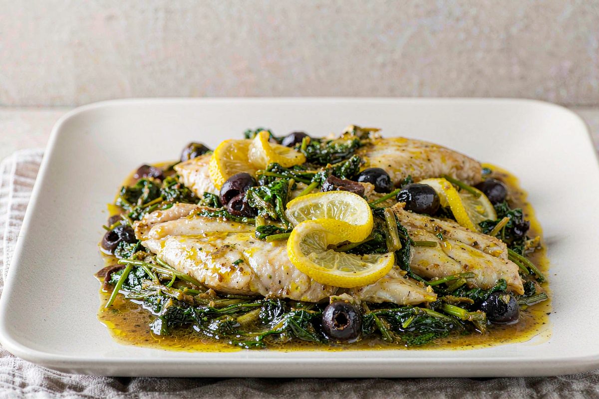 Baked cod fillets on a bed of wilted spinach with olives and lemon slices