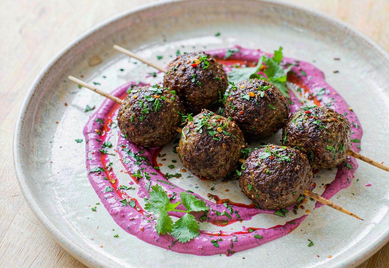 Spiced beef kofta on a plate drizzled with bright pink beet yogurt sauce