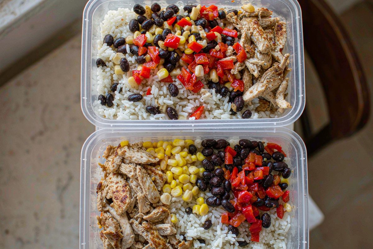 Meal prep containers layered with rice black beans chicken peppers and corn