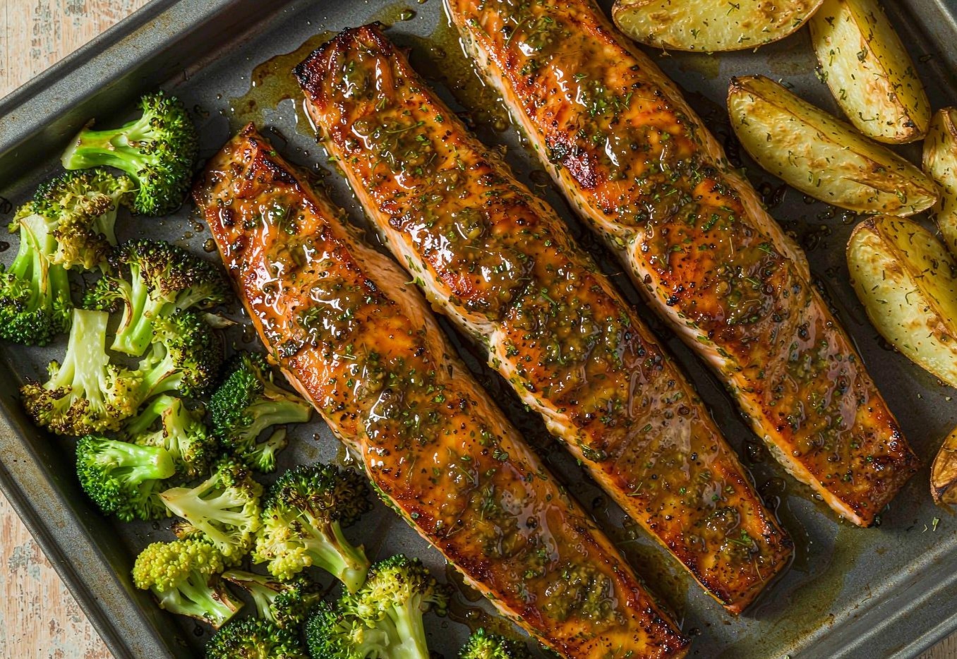 Glazed salmon fillets on a sheet pan with roasted broccoli and potato wedges