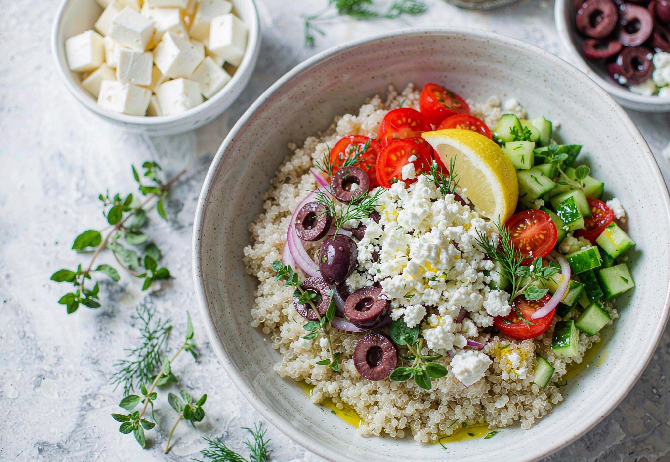Greek quinoa bowl topped with crumbled feta cucumber tomatoes and olives