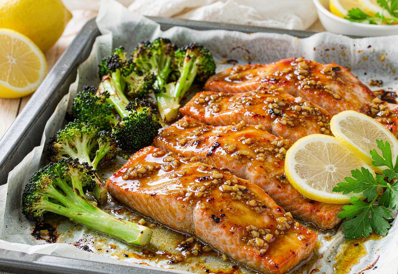 Baked salmon fillets with lemon slices next to charred broccoli on a sheet pan