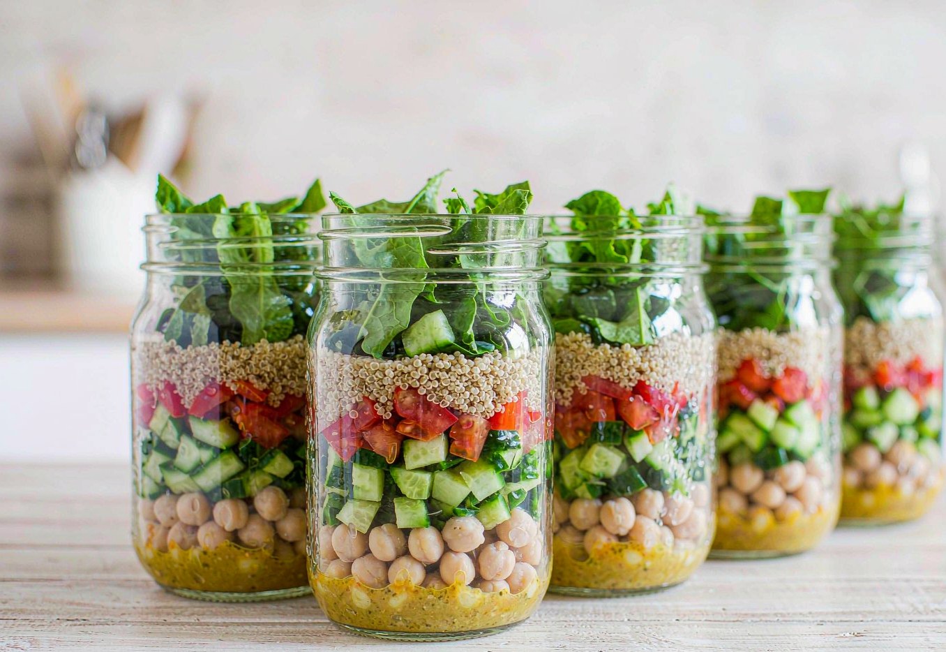 Five mason jar salads layered with dressing chickpeas vegetables and greens on top