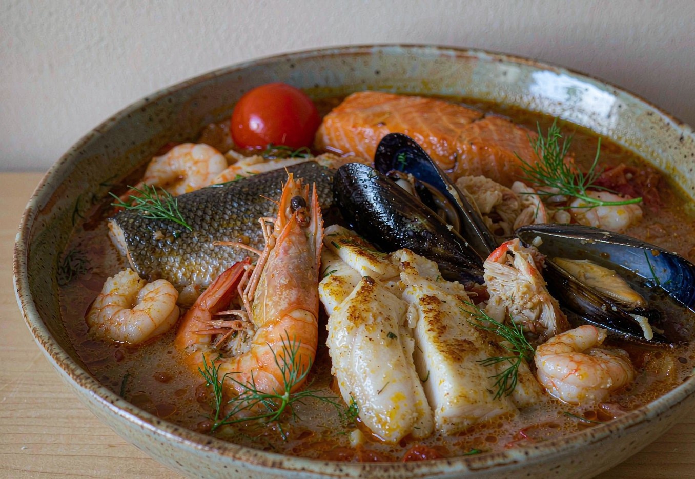 A pot of mixed seafood stew with salmon, cod, and shrimp in tomato broth
