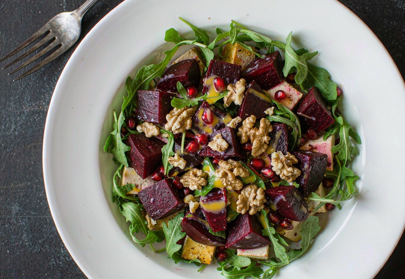 A bowl of roasted beet and tofu salad with arugula, walnuts, and citrus dressing