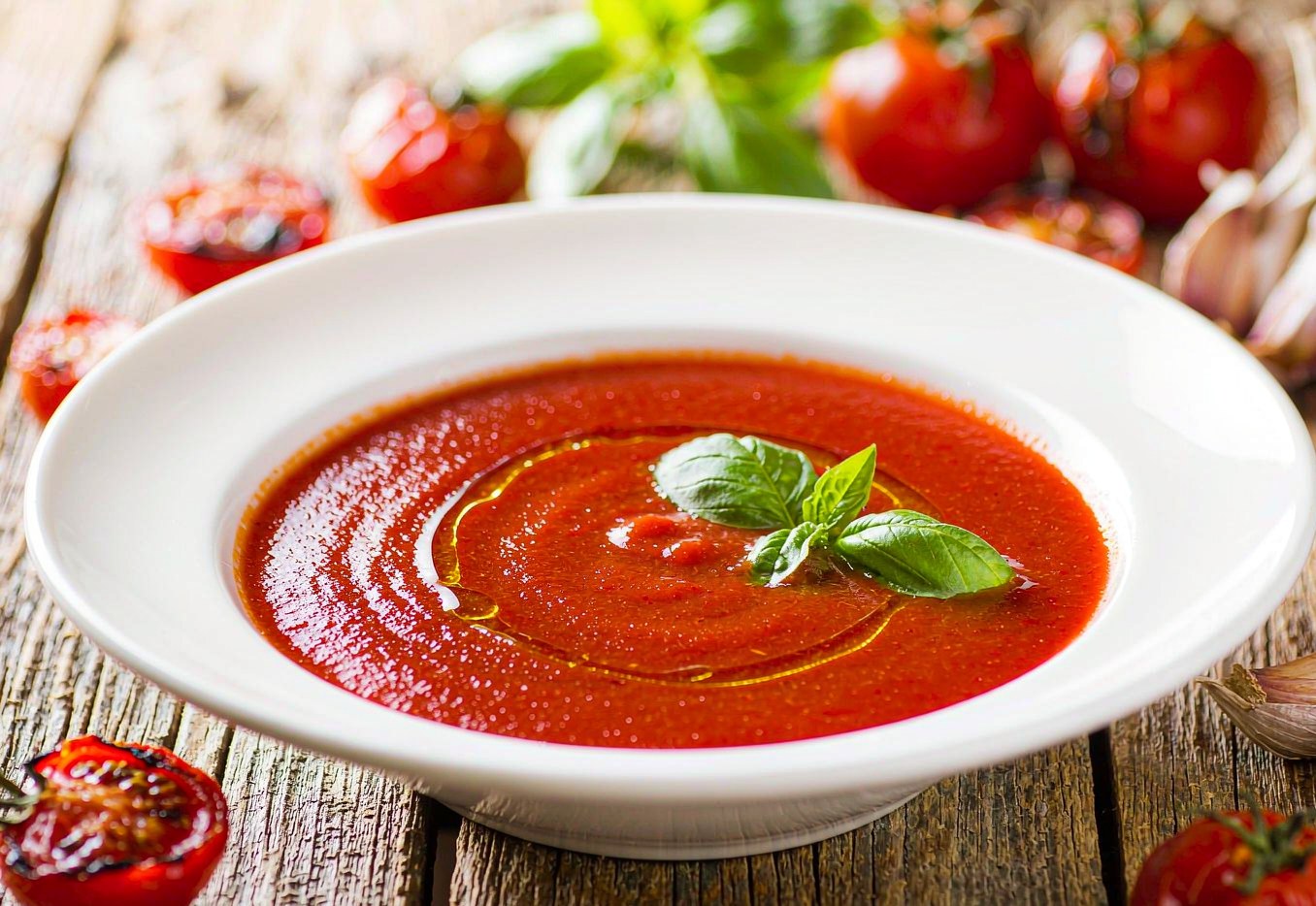 Smooth roasted tomato basil soup in a bowl with torn basil and olive oil